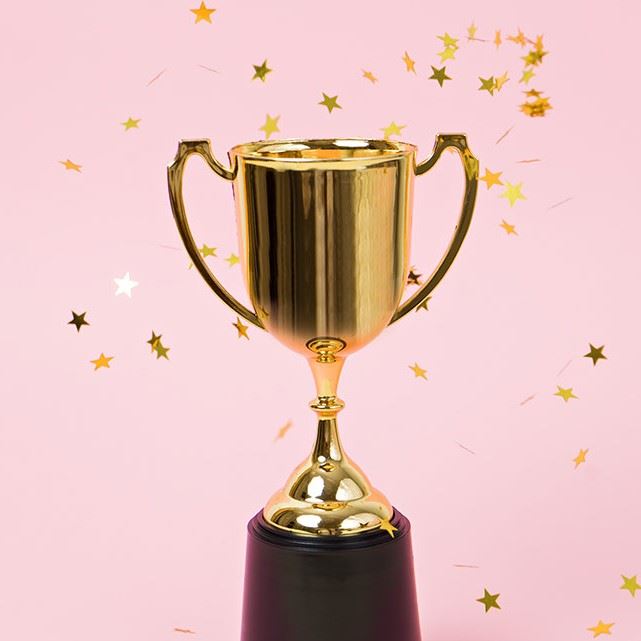 Image of gold trophy on a pink background with gold stars