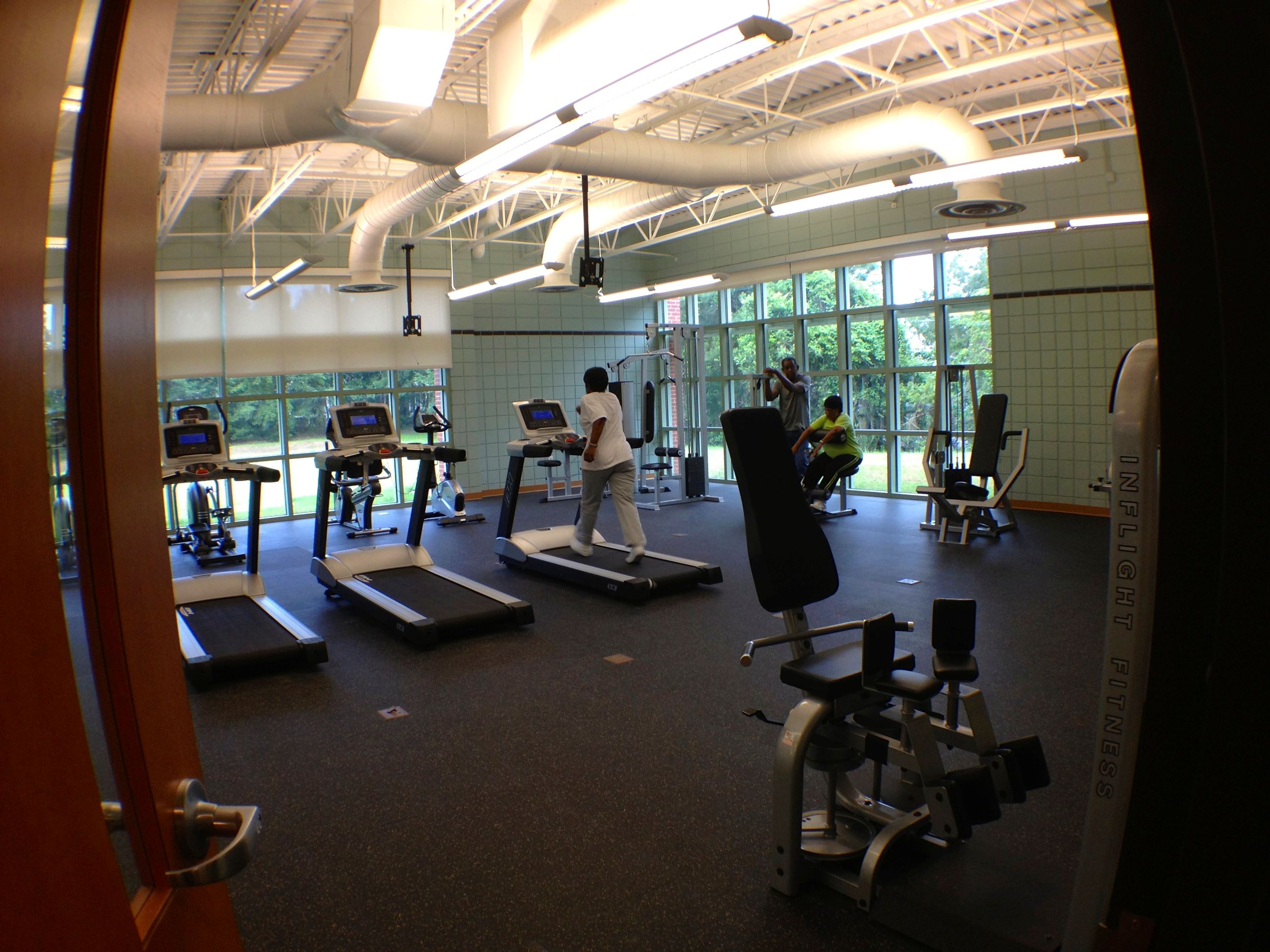 Three people exercising in a fitness room. One is on a treadmill, the others are weightlifting.