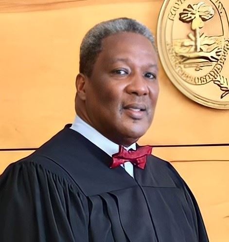 Pyatt stands in judge's robes in front of the judicial seal