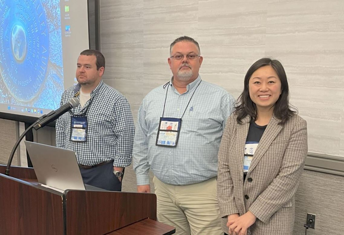 Three people stand by a podium in a hotel conference room.