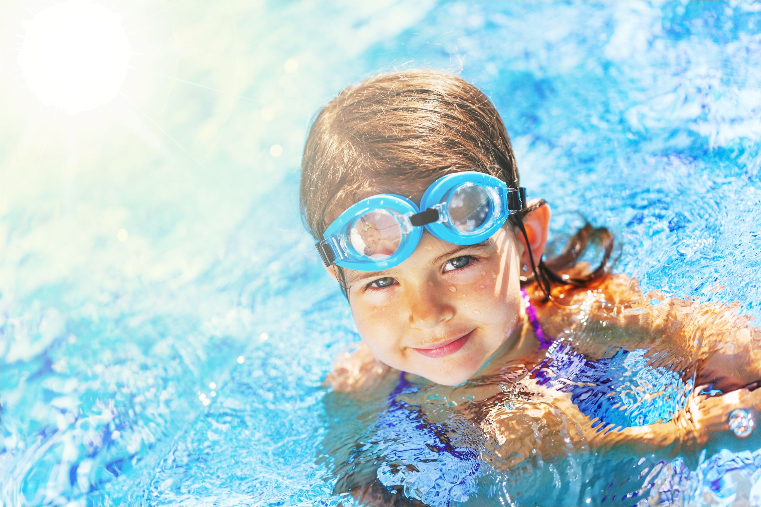 A smiling child with blue goggles on her head in a swimming pool