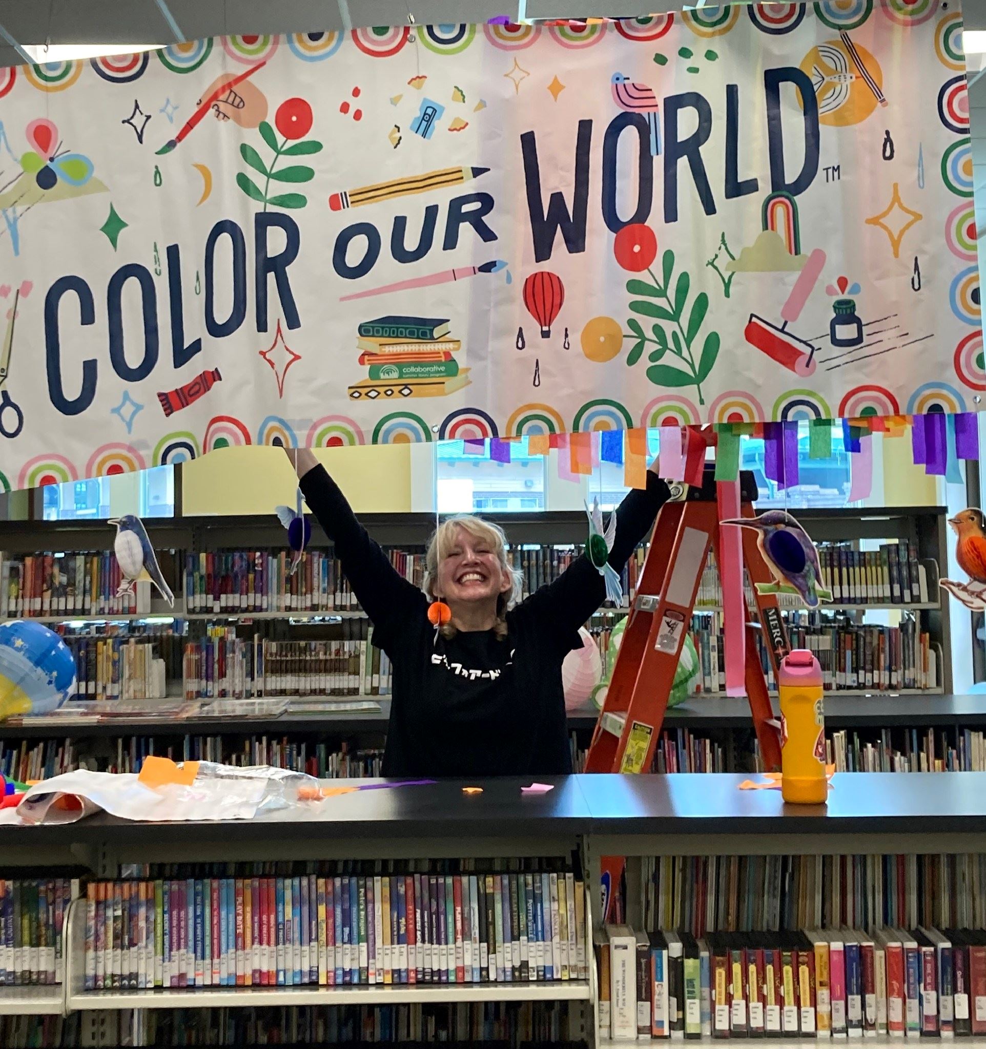 A female librarian cheerfully throws her hands in the air beneath a banner reading 