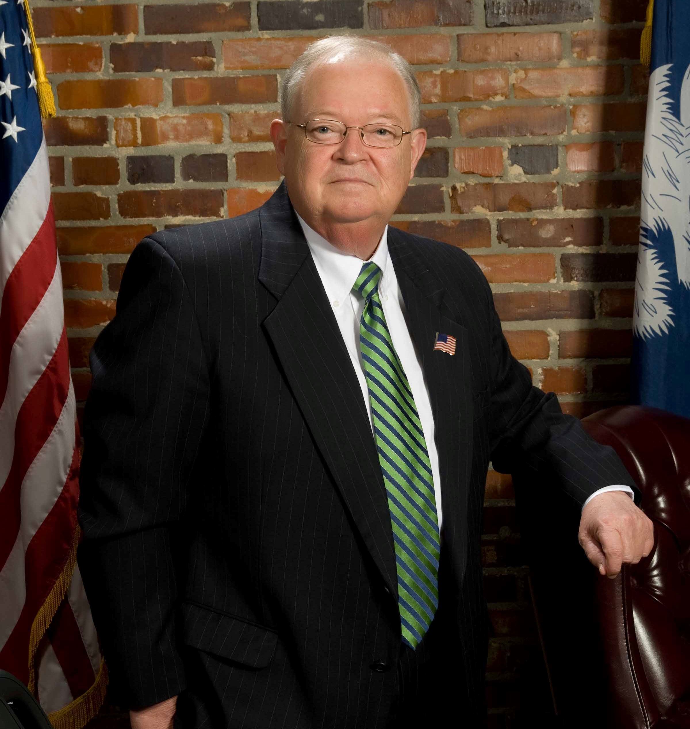 Portrait of A. Lane Cribb in a suit standing behind his desk with S.C. and U.S. Flag at his sides