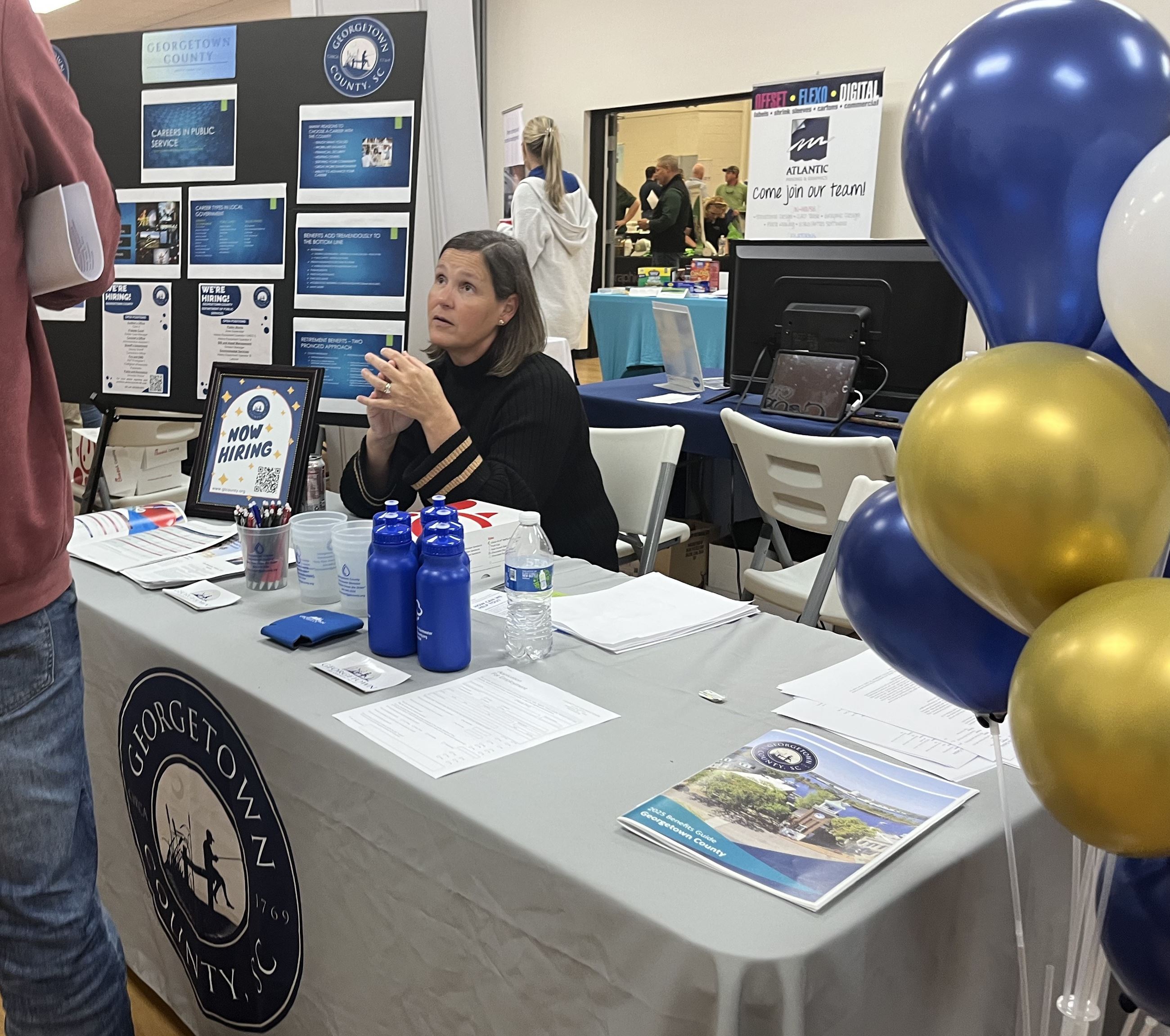 A cheerful woman sits behind a festively decorated table at a hiring event