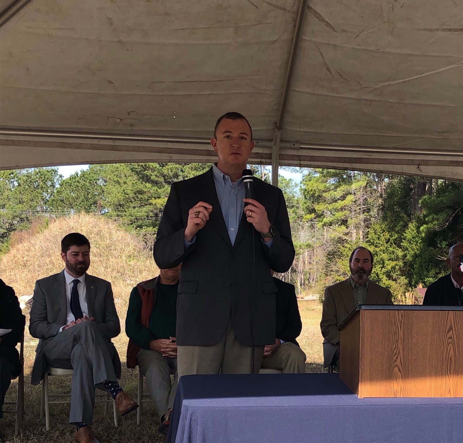 Brian Tucker, wearing a black blazer and blue shirt, gives a presentation at a groundbreaking.
