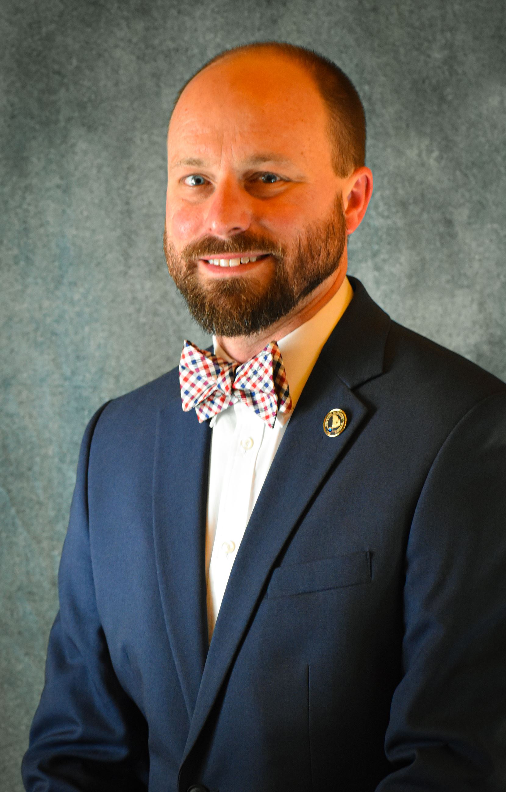Brandon Ellis, a Caucasian man wearing a navy blazer and red/white/blue bow tie, smiling.
